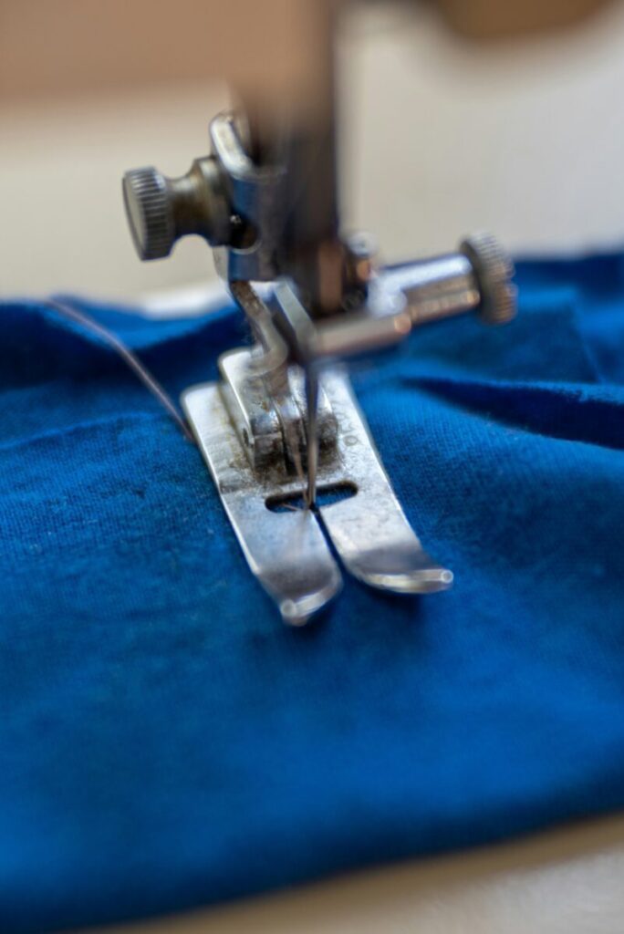 Close-up of a sewing machine needle stitching blue fabric, representing clothing manufacturing processes