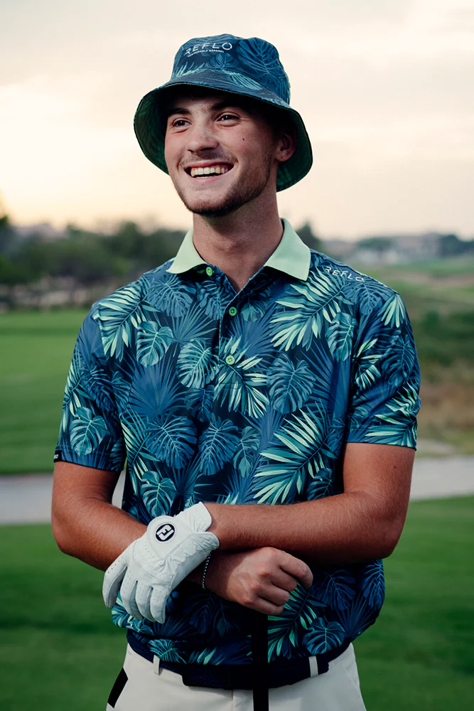 reflo-golf-apparel-doncaster-j-mitchell-design Male golfer wearing a tropical print Reflo golf shirt and matching bucket hat on a course at sunset, styled with a mint green collar and white golf glove