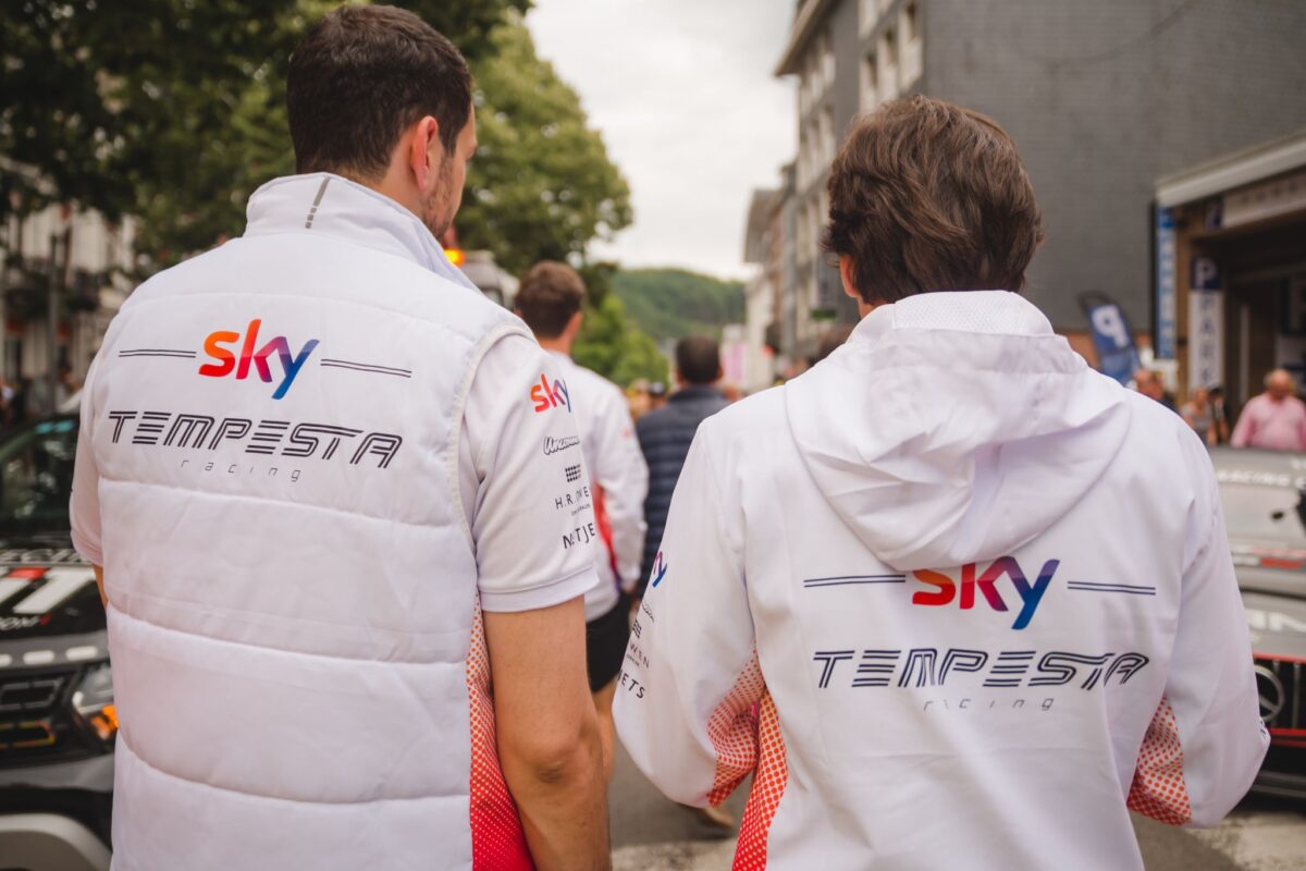 Sky Tempesta racing team members from behind wearing white branded gilets and hoodies at a motorsport event