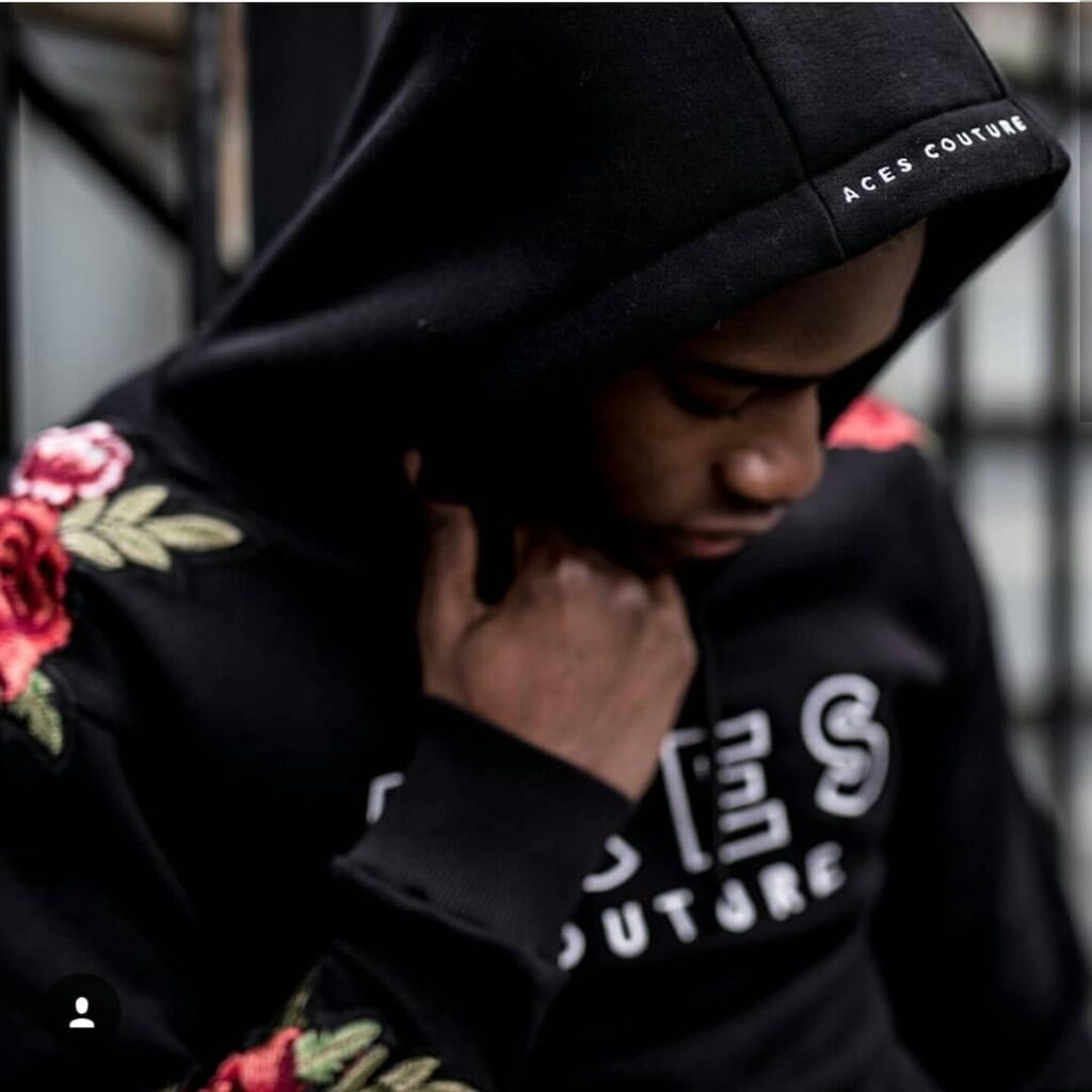 aces-couture-hoodie-embroidered-roses Man wearing a black hoodie with red rose embroidery and Aces Couture branding