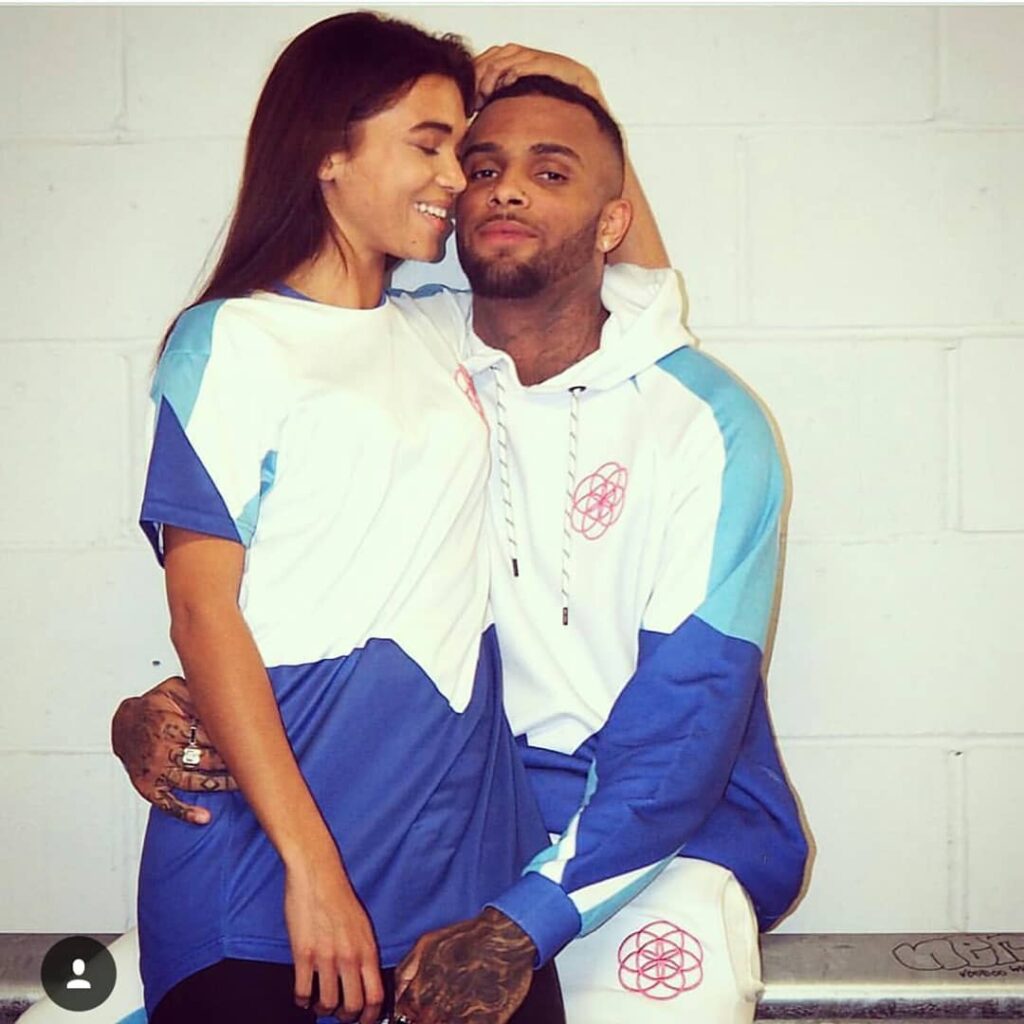 scar-tissue-blue-and-white-tracksuit-couple A couple wearing matching Scar Tissue blue and white outfits; the woman wears a colour-block tee, the man wears a coordinated tracksuit with pink geometric logo.