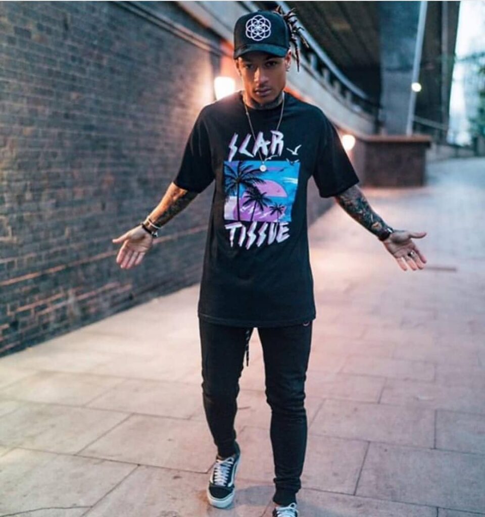 scar-tissue-graphic-tee-black-cap-night Male model wearing a Scar Tissue graphic tee and black cap, walking under an urban bridge at dusk.