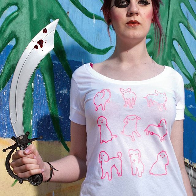 sloth clothing brighton graphic t-shirt designer Model in white T-shirt with pink dog illustrations holding a toy sword in front of a painted wall