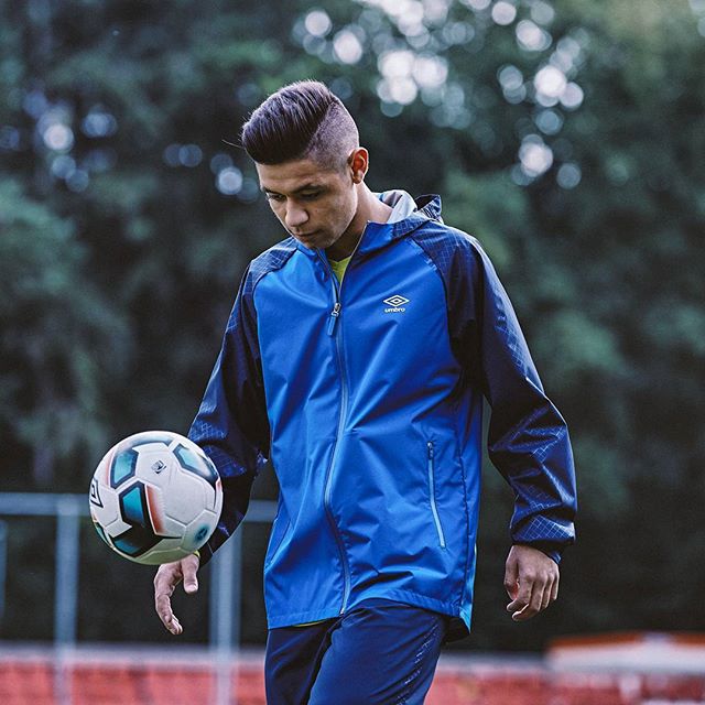 umbro-manchester-activewear-jacket-designer Footballer in blue Umbro jacket balancing ball on training pitch