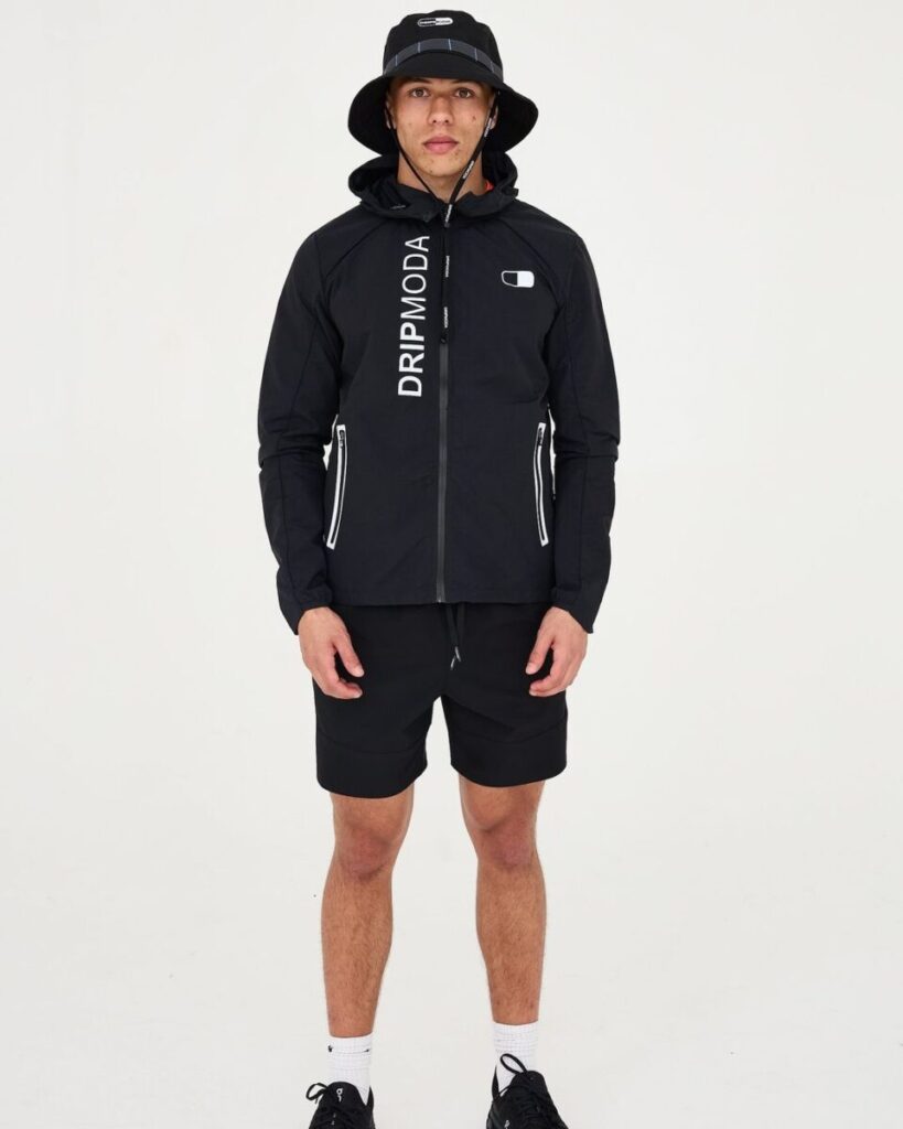 Dripmoda mountainwear jacket designer uk Model wearing full black streetwear look from Dripmoda SS2024 collection, featuring technical zip jacket with vertical logo, designed by J Mitchell Design.